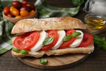 Tasty sandwich with mozzarella cheese, tomatoes and basil on wooden table, closeup