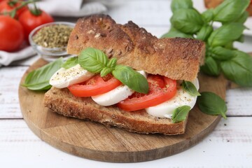 Tasty sandwich with mozzarella cheese, tomatoes and basil on white wooden table, closeup