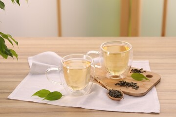 Tasty green tea in glass cups, brew and leaves on wooden table indoors
