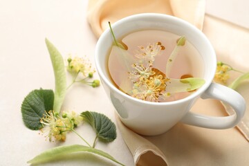 Fresh linden tea in cup and flowers on white table, closeup