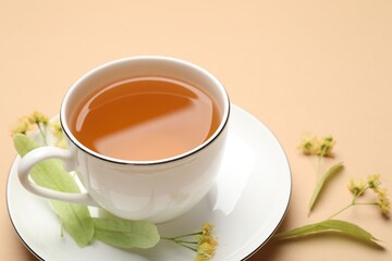 Tasty linden tea in cup, leaves and flowers on beige table, closeup
