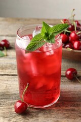 Tasty cherry soda with ice cubes, berries and mint on wooden table, closeup