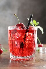 Tasty cherry soda with ice cubes, berries and mint in glass on wooden table, closeup