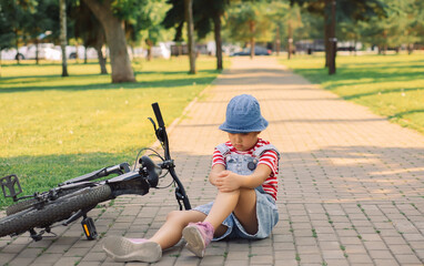 Teenager kid girl fell off a bicycle and injured her knee outdoors in park. Child sitting down on...