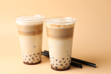 Tasty milk bubble tea in plastic cups on beige background, closeup
