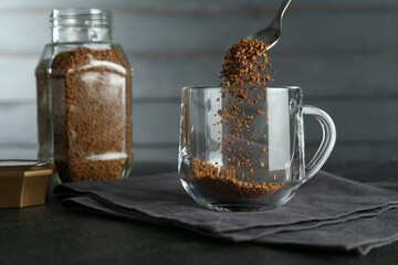 Putting instant coffee into cup at black table, closeup