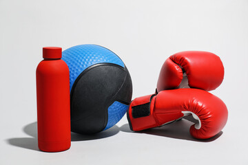 Medicine ball, boxing gloves and water bottle on light grey background