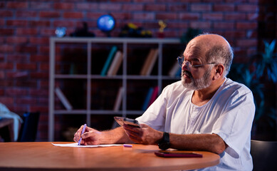 Elderly Indian man manages budget by counting cash and noting expenses at home