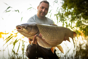 Fishing background. Young man hold big carp in his hands.