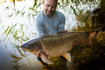 Fishing background. Young man hold big carp in his hands.