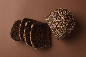 Pieces of fresh rye bread with seeds on brown background, flat lay