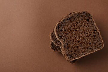 Pieces of fresh rye bread on brown background, top view. Space for text