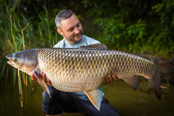 Fishing background. Young man hold big carp in his hands.