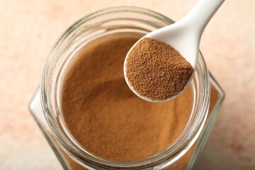 Spoon with instant coffee powder and jar on light table, above view