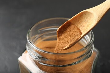 Adding instant coffee powder from spoon into jar on dark table, closeup