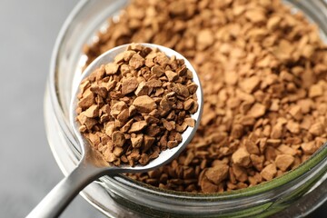 Spoon with granulated instant coffee and jar on grey background, closeup