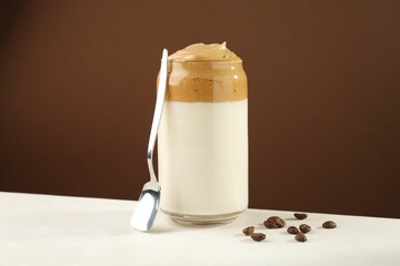 Delicious dalgona coffee in glass, beans and spoon on white table