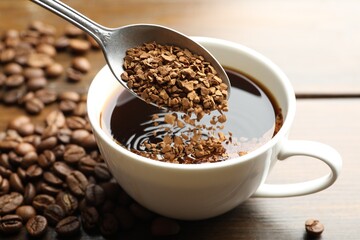 Putting instant coffee into cup of hot drink at wooden table, closeup