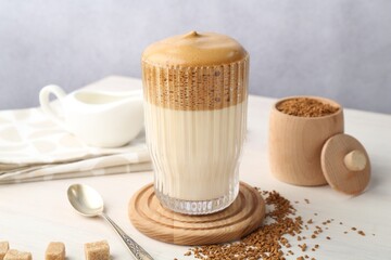 Delicious dalgona coffee in glass, granules and brown sugar on light table, closeup