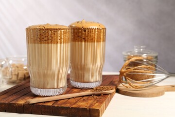 Delicious dalgona coffee in glasses, whisk, brown sugar and granules on light table, closeup