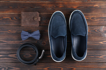 Pair of dark blue shoes, belt, bow tie and purse on wooden surface, flat lay