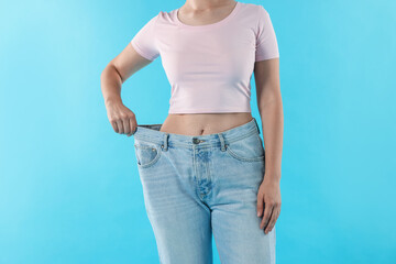 Woman wearing old jeans after weight loss on light blue background, closeup