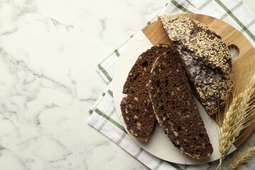 Pieces of fresh rye bread with seeds and spikes on white marble table, top view. Space for text