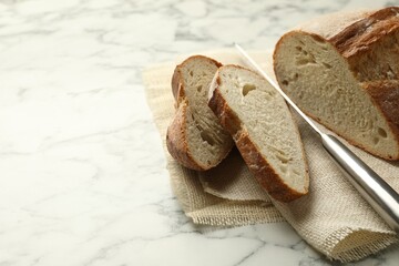 Pieces of fresh bread and knife on white marble table, closeup. Space for text