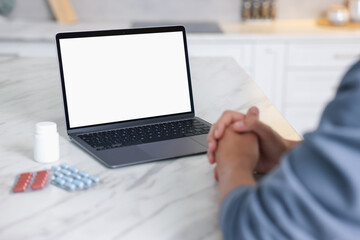 Man having online consultation with doctor via laptop at table in kitchen, closeup