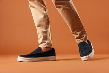 Man wearing pair of dark blue shoes on brown background, closeup