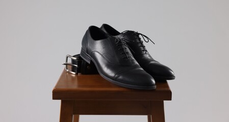 Pair of black leather shoes on stool against light background