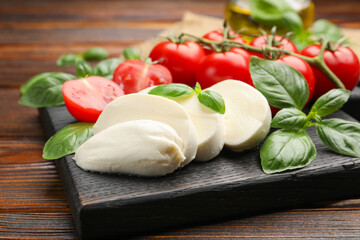 Tasty mozzarella cheese, tomatoes and basil on wooden table, closeup