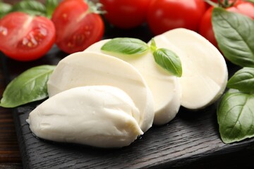 Tasty mozzarella cheese, tomatoes and basil on table, closeup