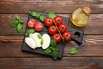 Tasty mozzarella cheese, tomatoes, basil and oil on wooden table, flat lay
