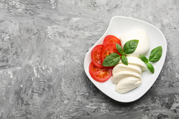 Tasty mozzarella cheese, tomato and basil on grey table, top view. Space for text