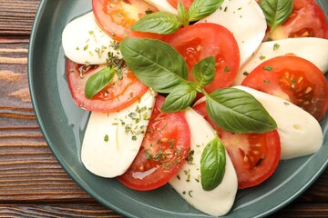 Tasty salad Caprese with mozzarella, tomatoes, basil and spices on wooden table, top view