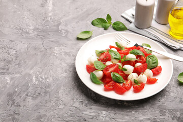 Tasty salad Caprese with mozzarella, tomatoes, basil and spices on grey table. Space for text