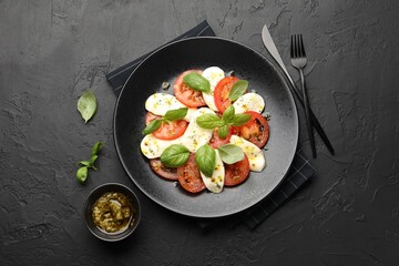 Tasty salad Caprese with mozzarella, tomatoes, basil and spices on black table, flat lay