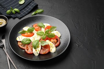 Tasty salad Caprese with mozzarella, tomatoes, basil and spices on black table, closeup. Space for...