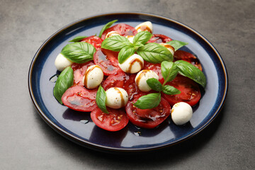 Tasty salad Caprese with mozzarella, tomatoes, basil and balsamic vinegar on grey table, closeup