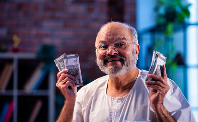 Elderly Indian man manages budget by counting cash and noting expenses at home