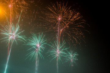 Colorful green and orange fireworks burst in the sky during an outdoor celebration, festival, or...