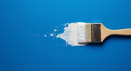 A paintbrush with white paint on a blue background creates a striking contrast, ideal for DIY and artistic projects.