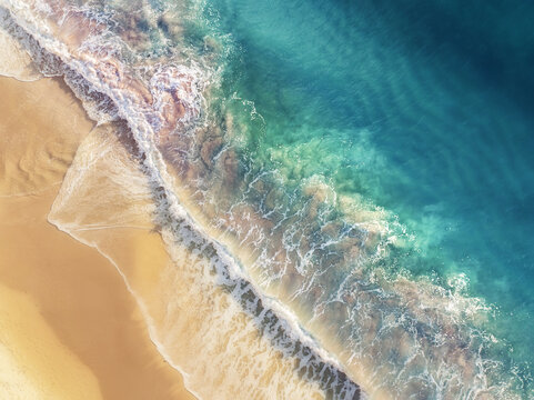 Aerial view of the shoreline's stark contrast where golden sands meet the turquoise ocean, the foamy waves creating a dynamic border, Port Willunga, South Australia, Australia.
