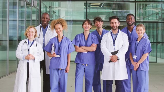 Camera tracks across faces of smiling medical team standing in modern hospital building looking into camera - shot in slow motion