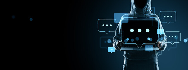 Hacker in hoodie holding laptop with digital chat bubbles on dark background, representing anonymous online communication and digital speech concept.
