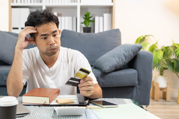 A man is sitting on the floor. He is looking at his credit card and checking his expenses on his...