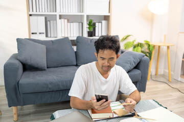 A man is sitting on the floor. He is looking at his credit card and checking his expenses on his...