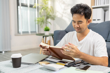 A man is sitting on the floor. He is looking at his credit card and checking his expenses on his...