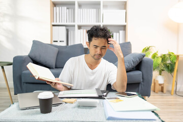 A man is sitting on the floor. He is looking at his credit card and checking his expenses on his...
